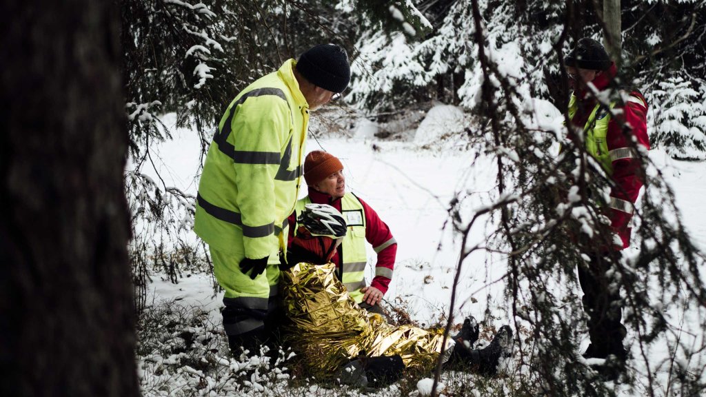 Yksi vapaaehtoinen istuu maassa avaruuslakanaan käärittynä. Kaksi seisoo hänen takanaan. Yksi seisoo kolmen edessä.